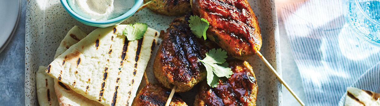 Skewers of grilled chickpea koftas on a speckled plate with grilled pita triangles and flecks of fresh coriander.