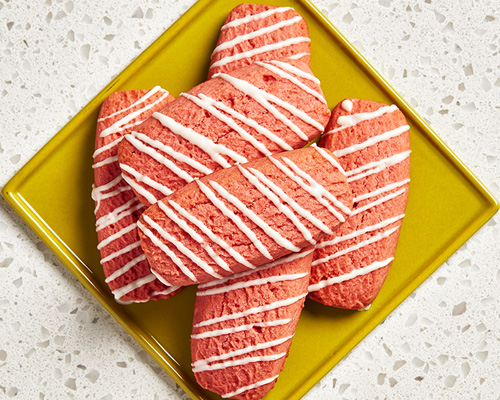 Pink rectangular-shaped cookies drizzled with icing sitting on a yellow plate.