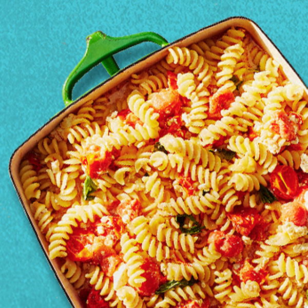  White baking dish filled with fusilli pasta, baked cherry tomatoes and feta cheese.