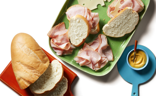 talian deli meats, a wheel of brie, and sliced baguette rounds on a blue serving platter with a cheese knife next to it on a white countertop.