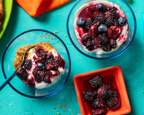 Berry topped cheesecake parfait cups on top of a blue counter top.