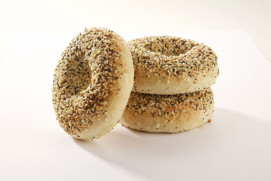 Three everything bagels, two stacked on top of each other with one leaning against it on a white board.