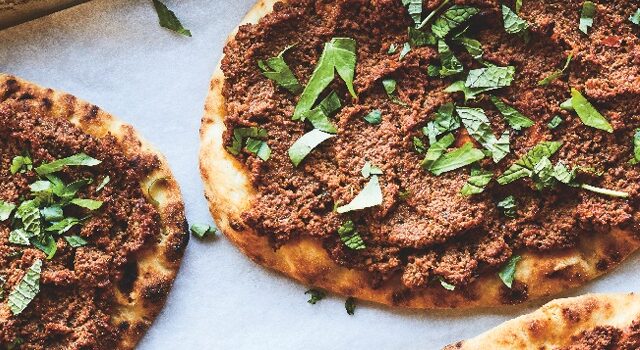 Baking sheet with four meat-topped flatbreads garnished with fresh mint and parsley