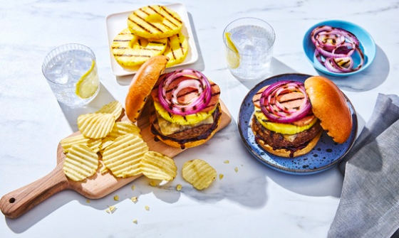 Two Hawaiian-inspired burgers with grilled pineapple rounds and a side of ruffled plain potato chips