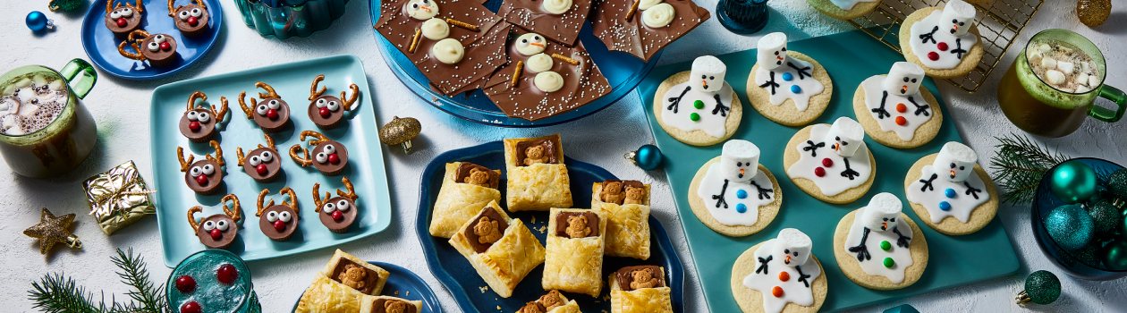 Overhead shot of cute sweet snacks including melting snowman, snowman bark, reindeer peanut butter cups, and sleeping teddy bears.