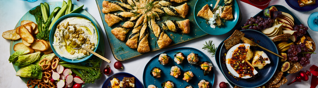 Overhead shot of crowd pleasing appetizers include spanakopita twists, sushi bake cups, baked brie, and more