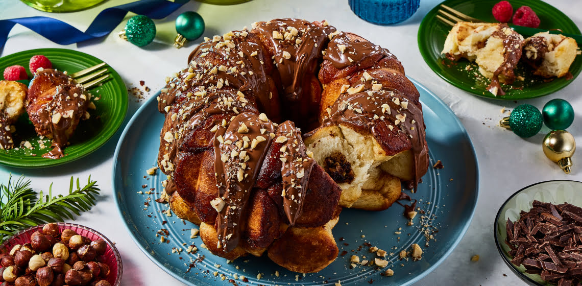 Chocolate hazelnut monkey bread on plate with hazelnuts on bowl to the side.