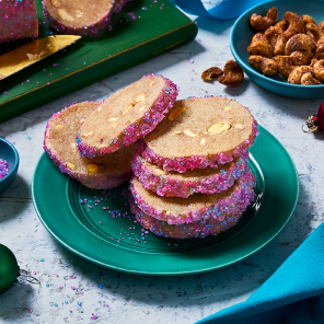 A log of icebox cookie dough on a board with a few cut off beside a teal plate stacked with more icebox cookies