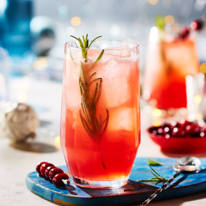 Cranberry Paloma in a highball glass on a white marble surface scattered with holiday decorations.