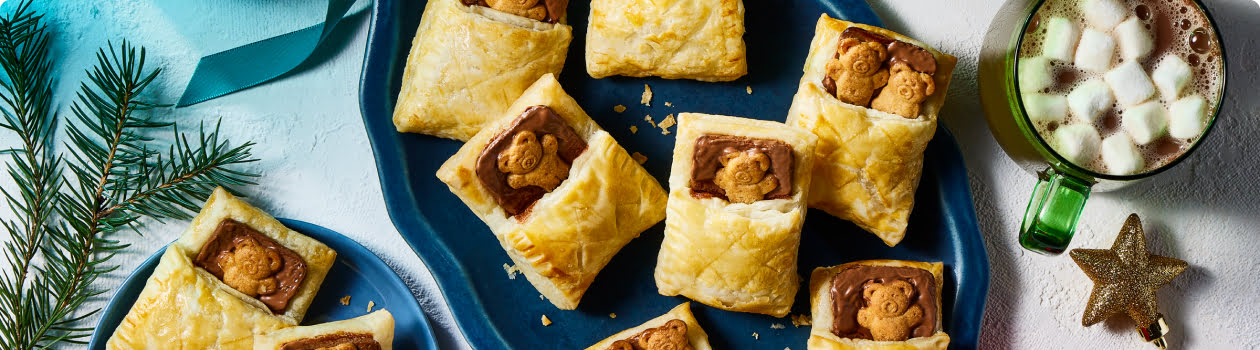 Puff pastry filled with chocolate and teddy cookies on a platter with cups of hot chocolate on to the side