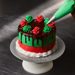 Green and Red Iced Cake with dripping chocolate ganache and red and green rosettes being added to the cake