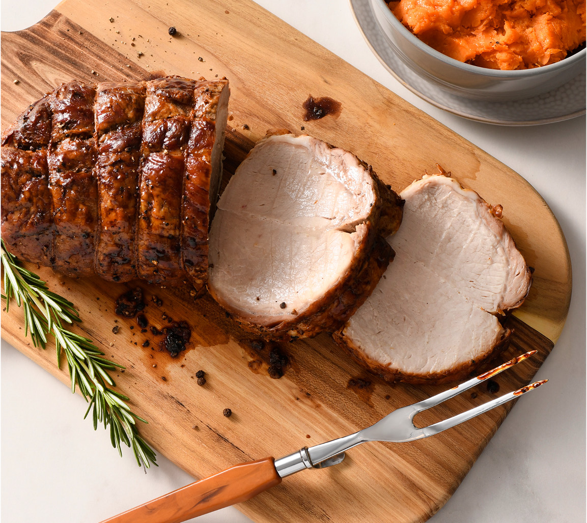 Sliced boneless pork loin rib roast on cutting board with side of mashed sweet potatoes