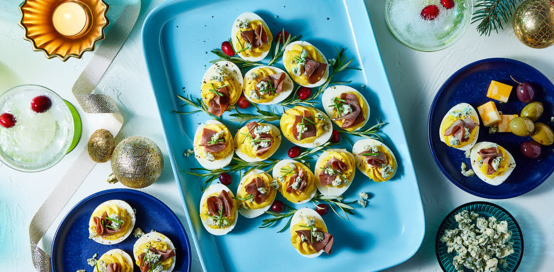 Plate of deviled eggs placed in a shape of a Christmas tree topped with roast beef and blue cheese