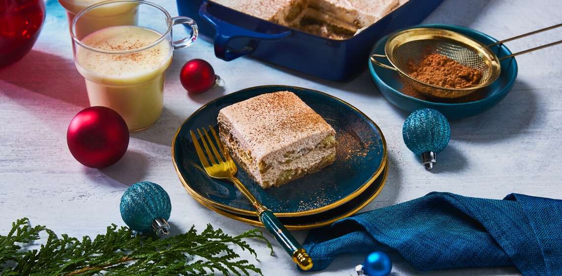 Eggnog tiramisu in a blue baking dish with slice of tiramisu on blue plate