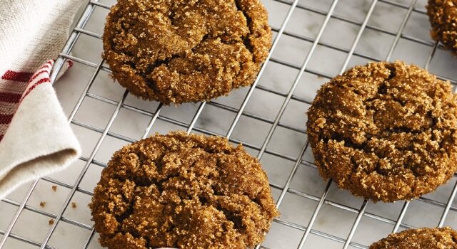 Chewy ginger molasses cookies on a cooling rack and in a white bowl on a white countertop