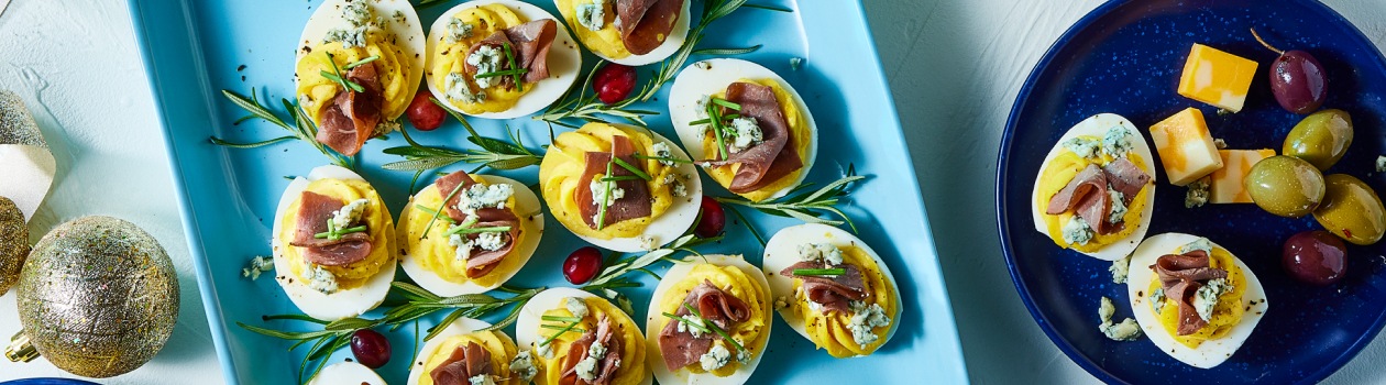 Plate of deviled eggs placed in a shape of a Christmas tree topped with roast beef and blue cheese