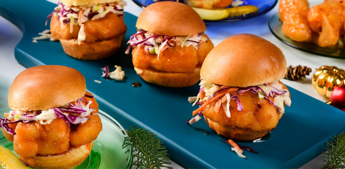 One hot honey cauliflower sliders with pickle ranch slaw on a green plate and three on a blue serving plate