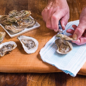 Man shucking oysters on cutting board