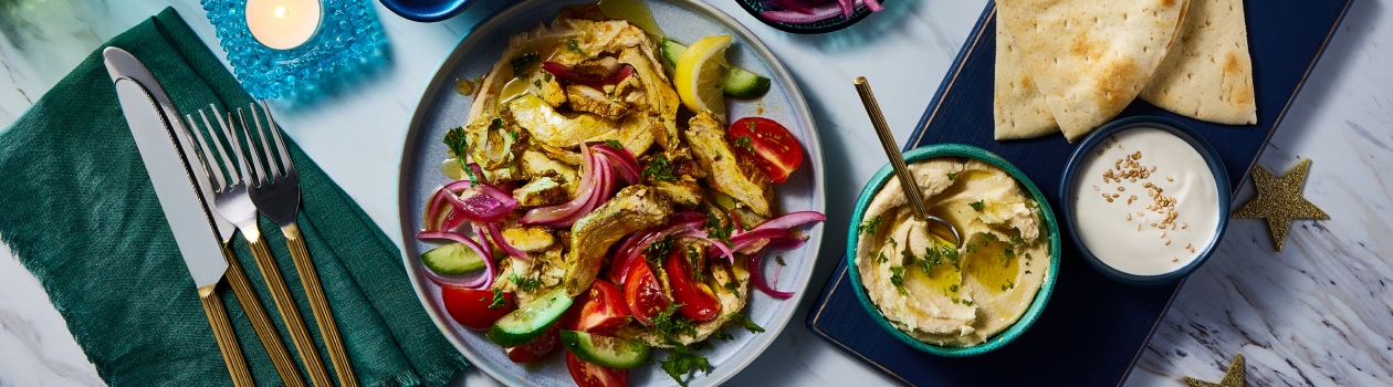 Chicken shawarma on a plate with tomatoes, onion and cucumber slices. Loaf pan beside