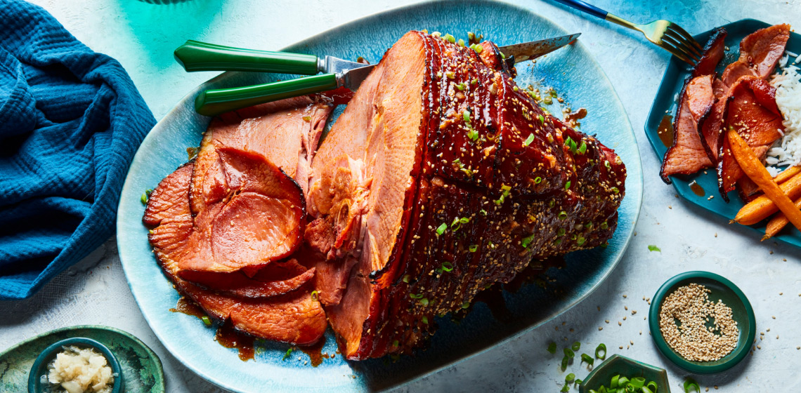 Oval light blue platter with Gochujang & Maple Glazed Spiral Ham with sesame seed and green onion garnish