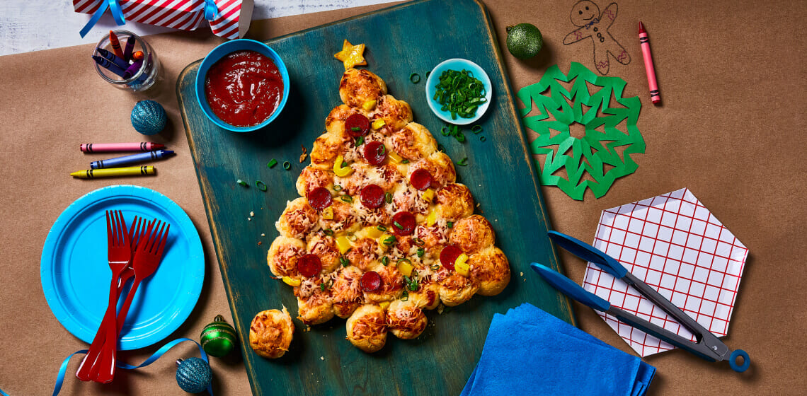 PIzza buns shaped into a Christmas tree topped with pepperoni and peppers on a blue cutting board.