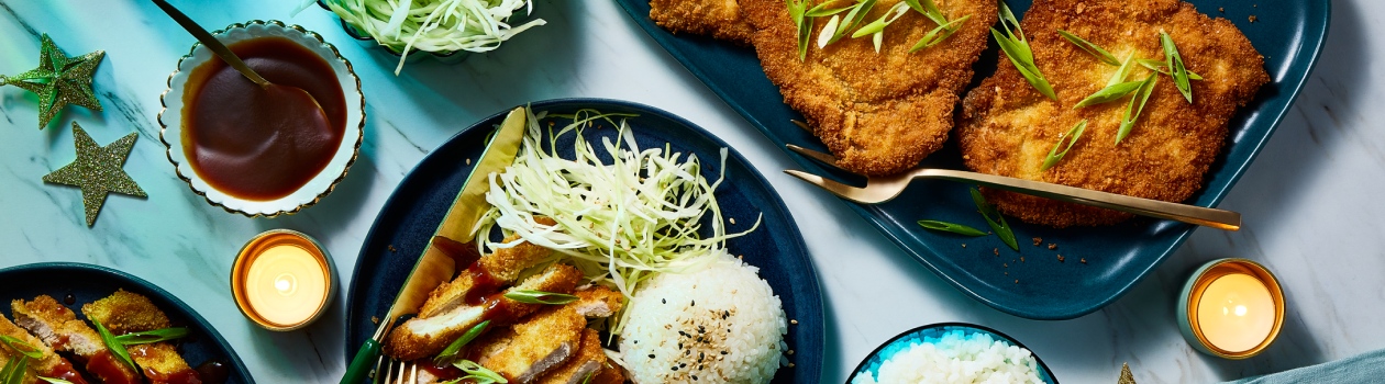 Sliced pork katsu on blue plate with a side of rice. Full pieces of katsu to the side on a blue serving platter