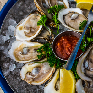 Shucked oysters on a bed of ice with dip and fork