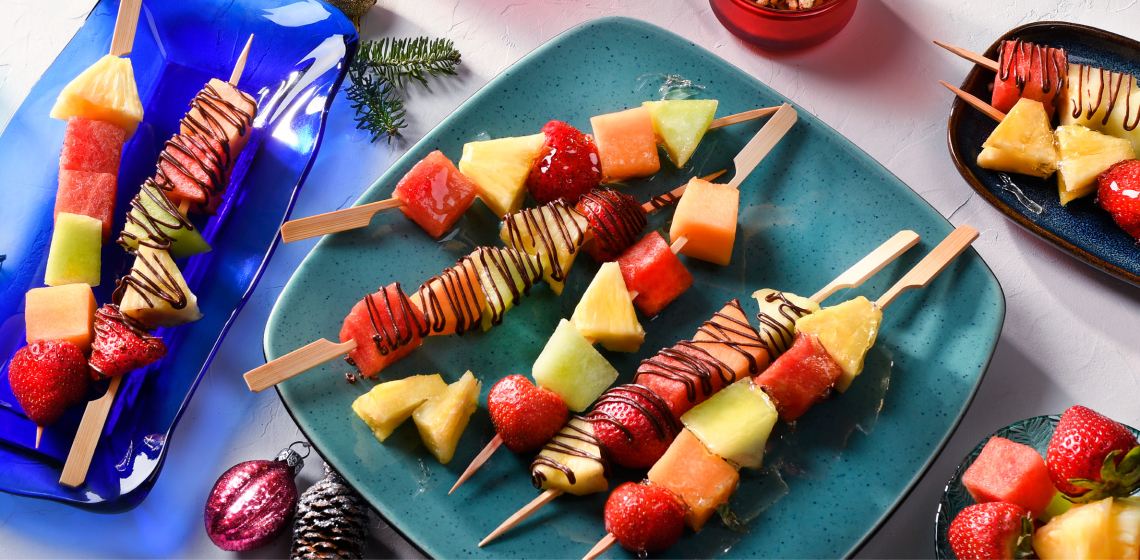 5 fruit skewers with chocolate drizzle on a blue plate