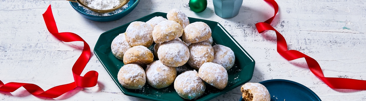 A stack of snowball cookies on a plate and a small plate with a full cookie and one that has a bite out of it