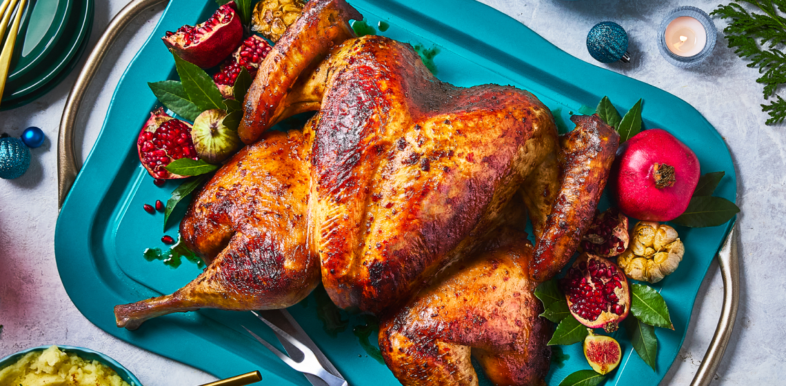 A spatchcock turkey on a teal serving platter with herbs and fruit