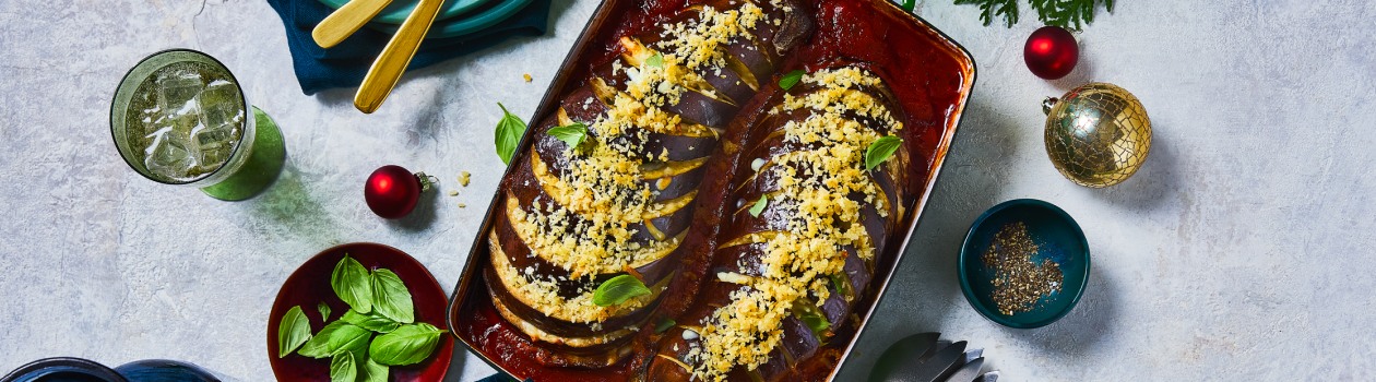 Two hasselback eggplants in a tray covered with cheese and sauce.