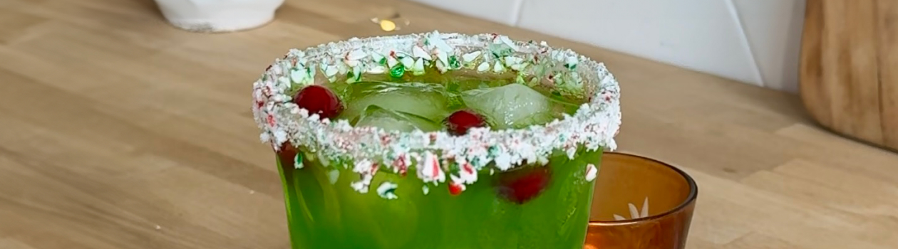 Mean green cocktail in glass with peppermint rim and candy canes in plate beside glass