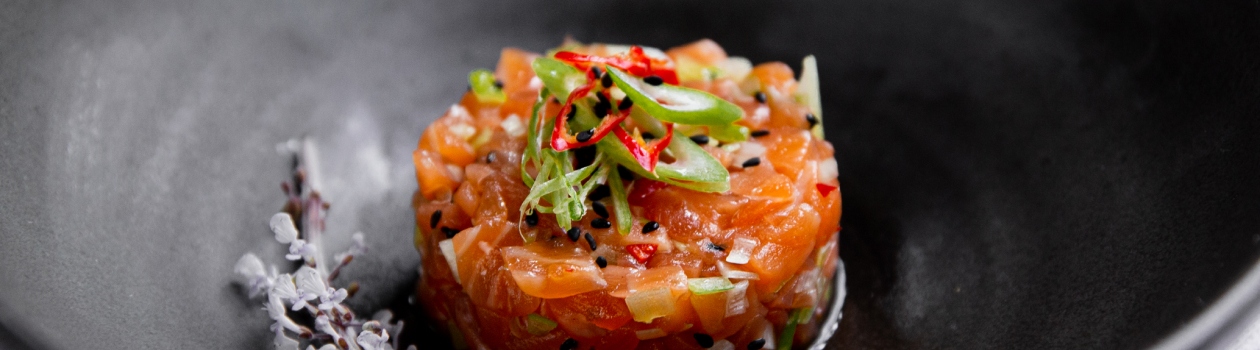 Salmon tartare in the centre of a black plate