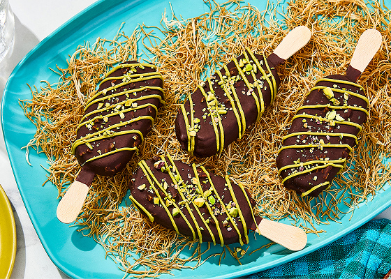 Four Dubai Inspired Chocolate Pistachio Bars on a bed of kataifi with one bar off to the side with a bite taken out and a bowl of pistachios.
