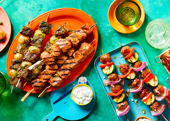 A variety of skewers on orange and blue plates on a green background.