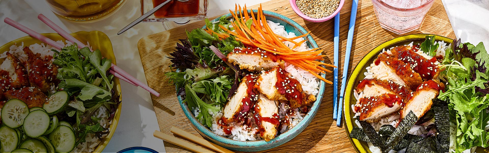 Korean chicken rice bowls topped with thinly sliced carrot, and sesame seeds.