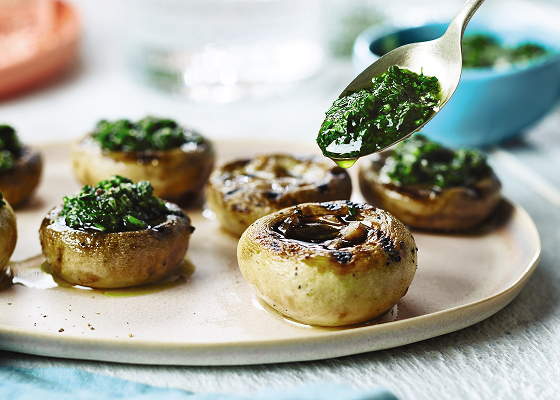 Seven grilled pesto-filled mushrooms on a white plate.