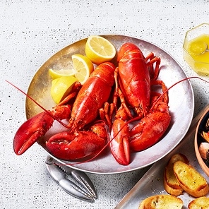 first-of-the-season-lobster Full cooked lobster in a bowl beside a plate of toasted bread.