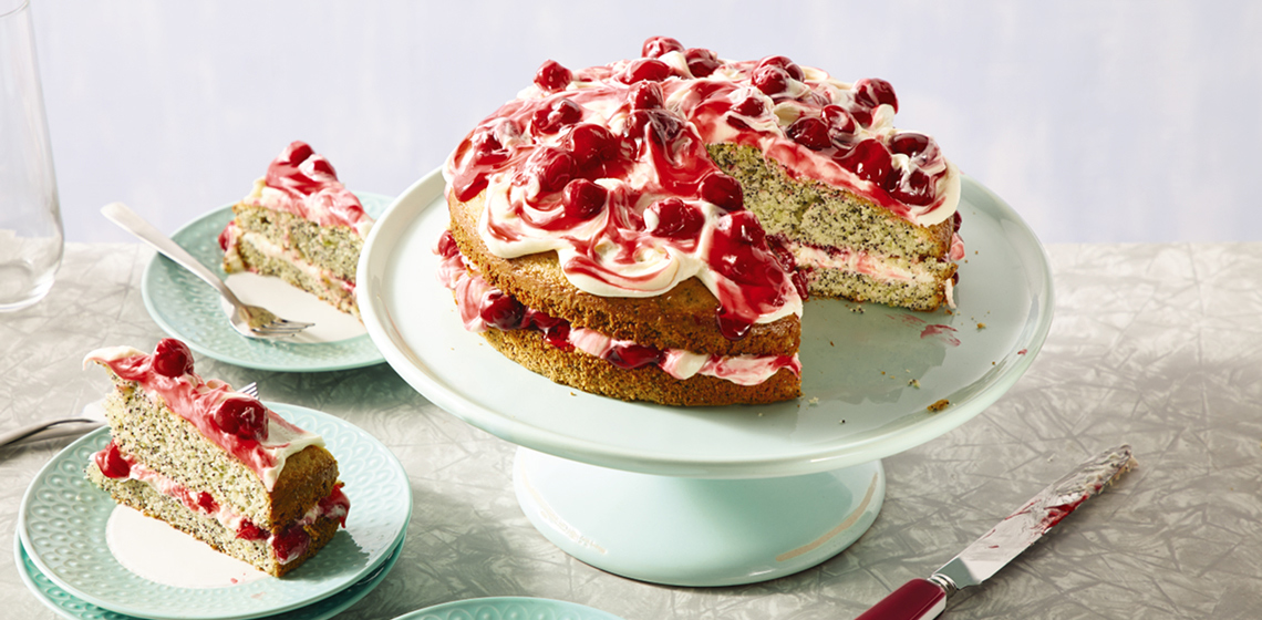 Cherry poppy seed cake on a blue cake stand with a slice cut out, next to two slices of cherry poppy seed cake on blue and white plates.