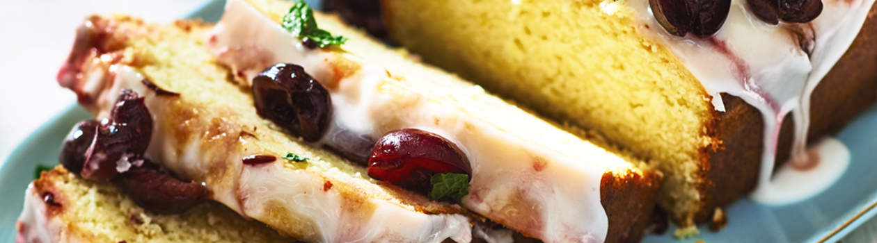 Sliced glazed lemon half-pound cake with cherries on a blue plate.