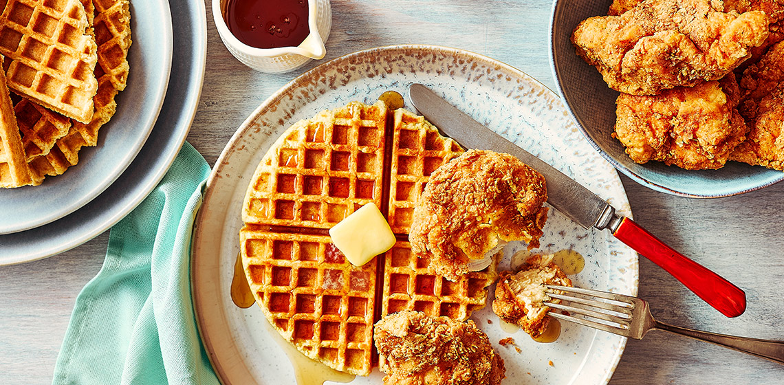 Fried chicken and bannock waffle on a white plate, with a plate of fried chicken and a plate of bannock waffles on the side.