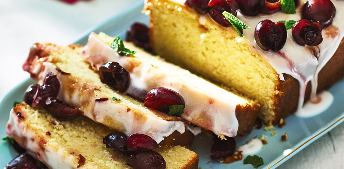 Sliced glazed lemon half-pound cake with cherries on a blue plate