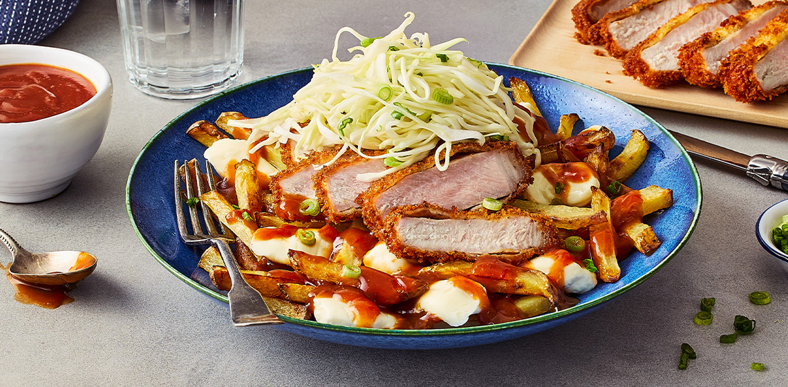 A bowl with the Japanese Tonkatsu Poutine, a cutting board with slices of the pork cutlet, a bowl of green onion, and another bowl of the tonkatsu-style gravy.