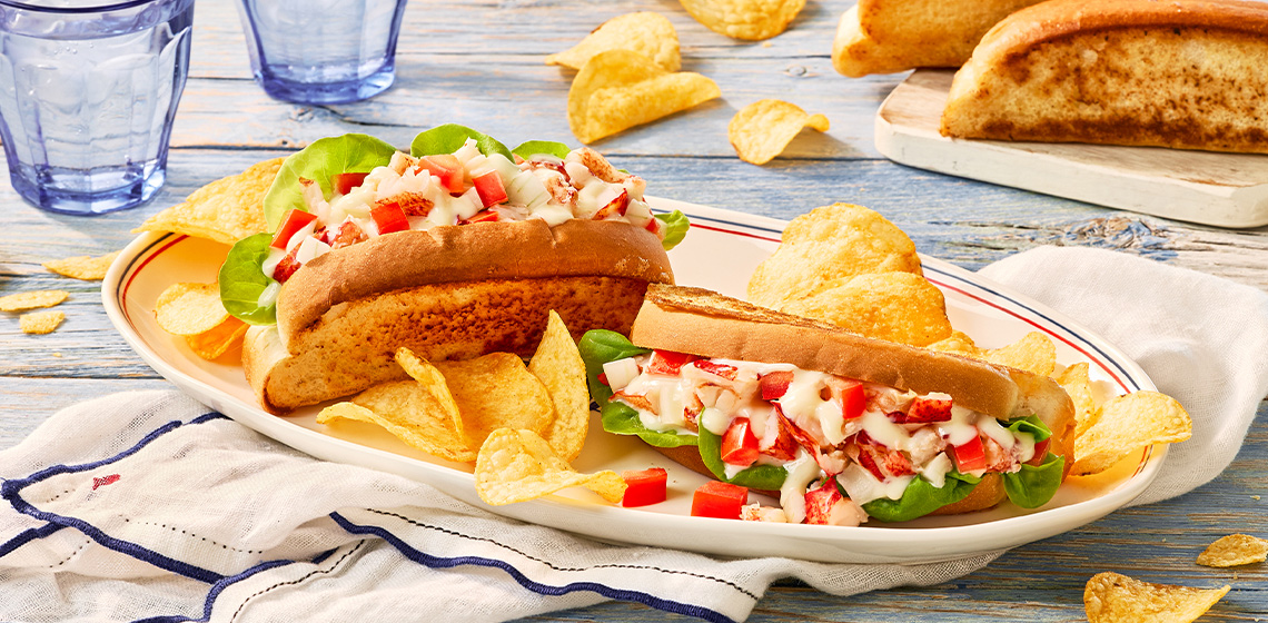 Two lobster rolls on a plate topped with Donair sauce with a side of chips