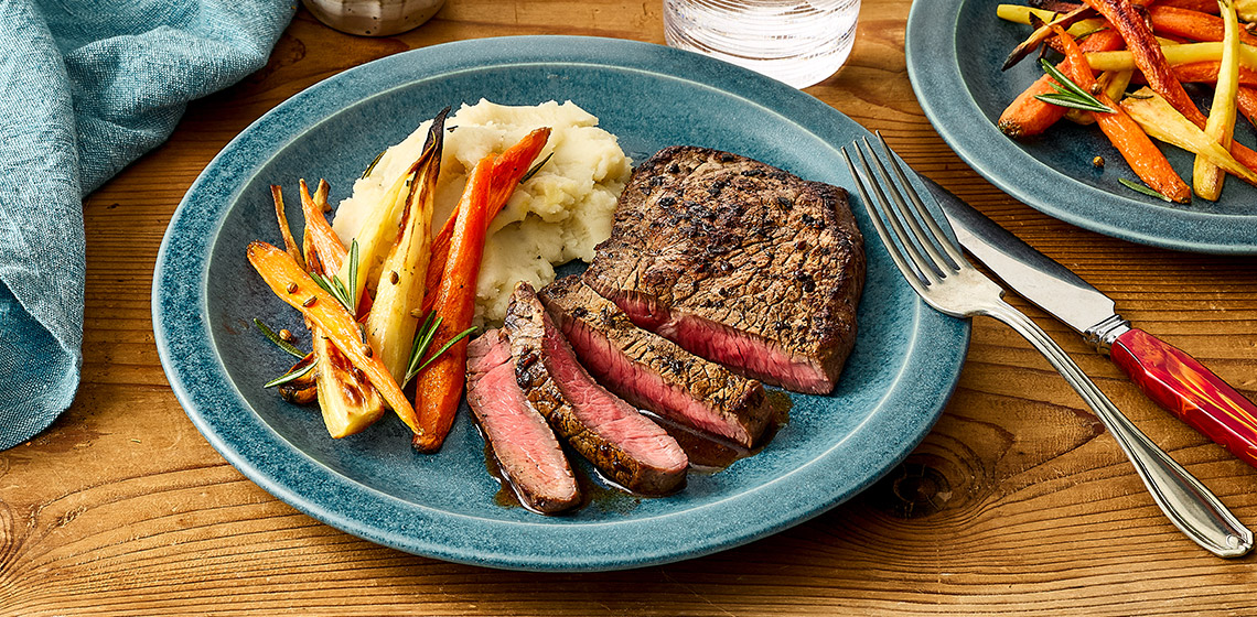 Sliced bison sirloin steak with mashed potatoes and roasted carrots.