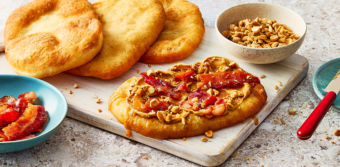 Sweet pastry topped with peanut butter, and maple candied bacon on a cutting board.