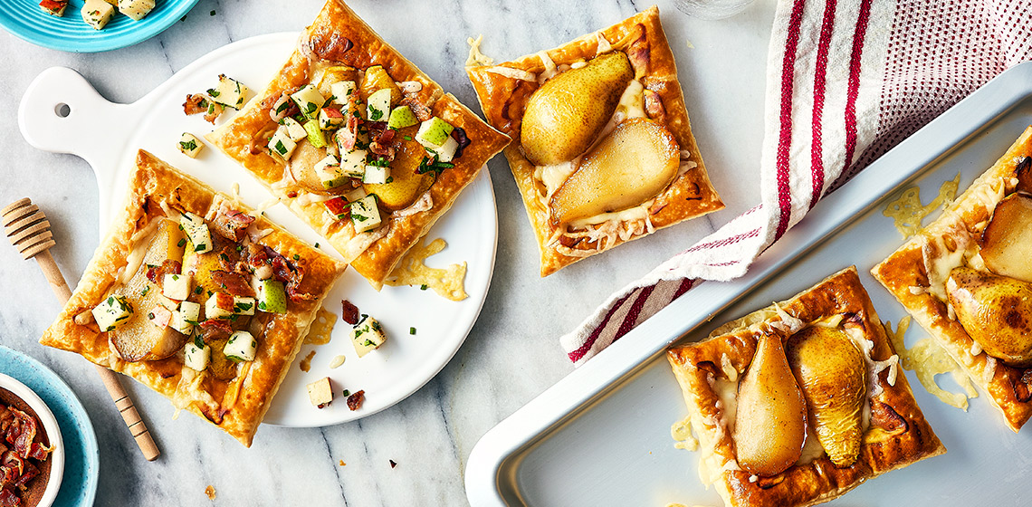 Three pear puff pastry tartlets on a plate, with two off to the side on a baking sheet.
