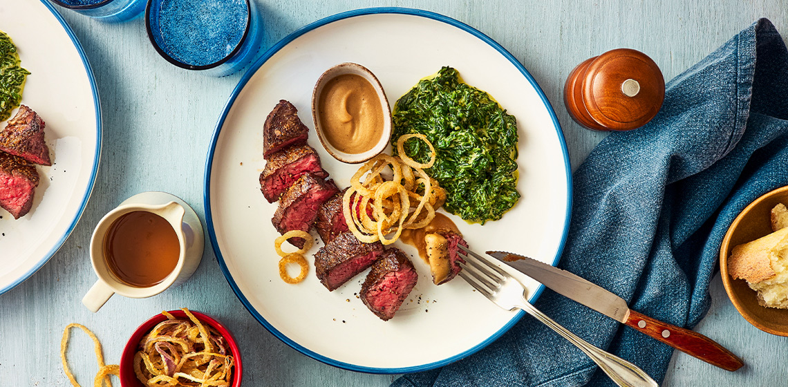 Sliced steak on white plate with side of creamed spinach