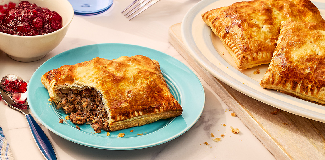 Tourtiere hand pie on a blue plate with a platter beside it.