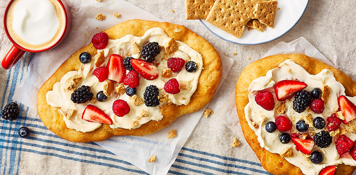 Two sweet fried pastries topped with cream cheese icing, fresh berries, and graham crumbs.